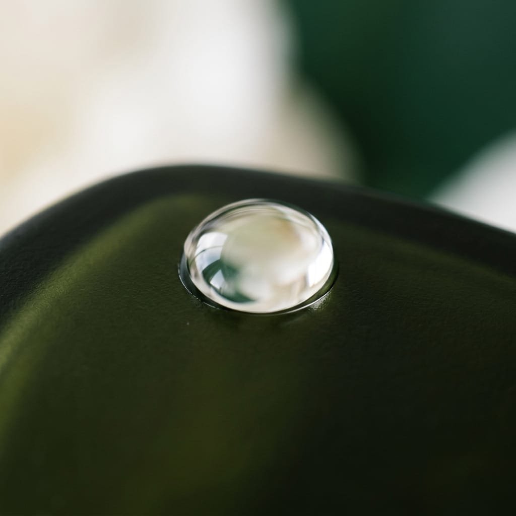 A single clear droplet resting on a deep green glossy surface